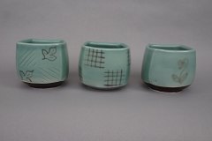 Trio of pseudocubic tea bowls: thrown then altered porcelain, celadon glaze with sassafras, woven, and lily-of-the-valley motifs brush applied with pseudocubic hematite slip, cone 6 oxidation