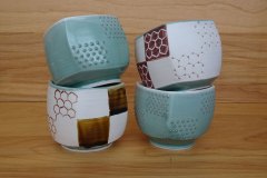 A stack of pseudocubic teabowls: thrown then altered porcelain with circular trimmed feet.  Hexagonal lattice motifs made with hematite slip, celadon and amber glazes.